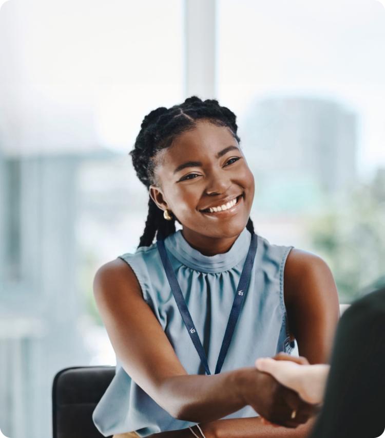 jeune femme souriante, dans une ambiance corporate, serrant la main à quelqu'un hors caméra